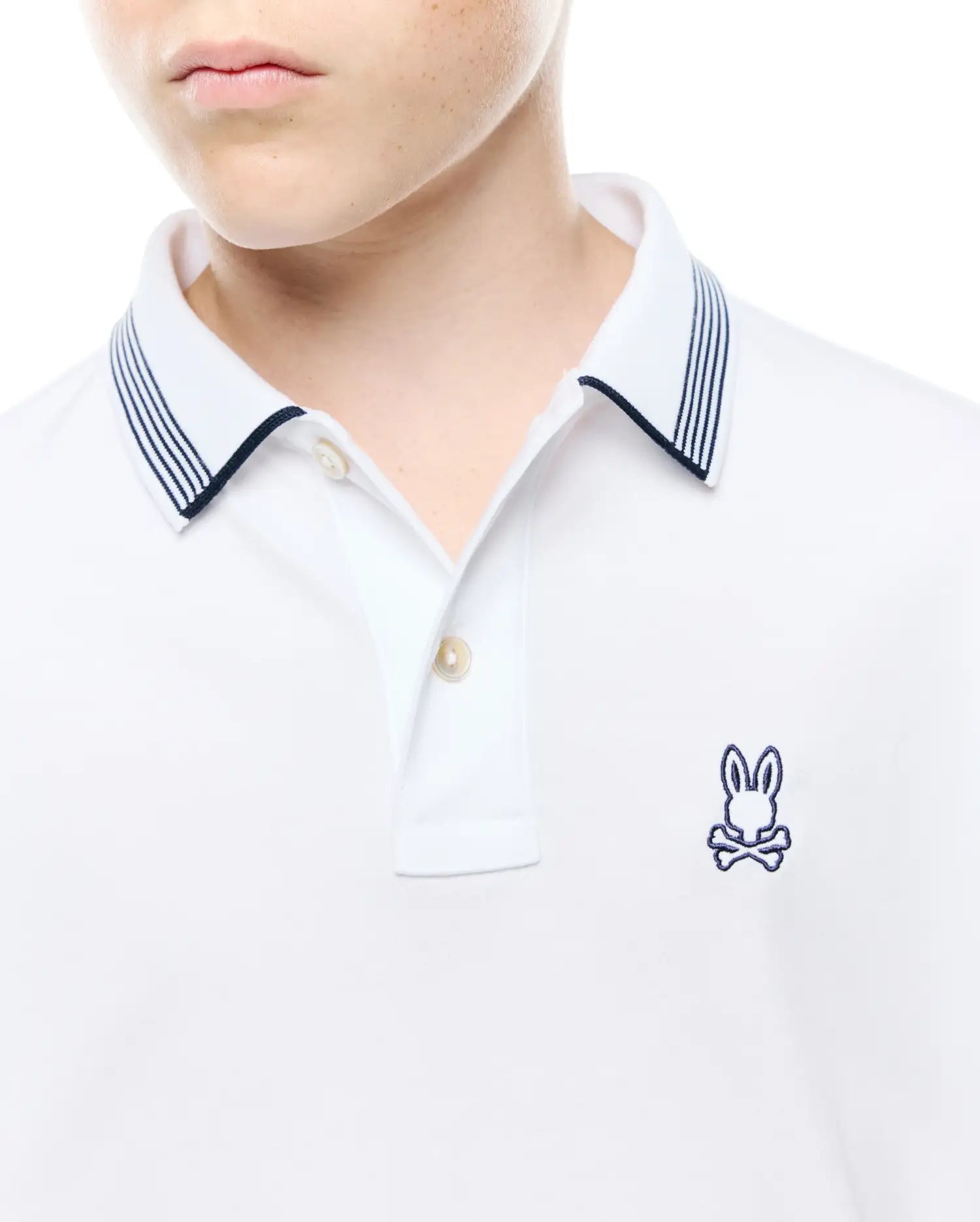 Kids Timmy Pique Polo, a classic white pique polo featuring a two-button placket, navy blue striped collar, and a small embroidered Psycho Bunny skull logo on the left chest.