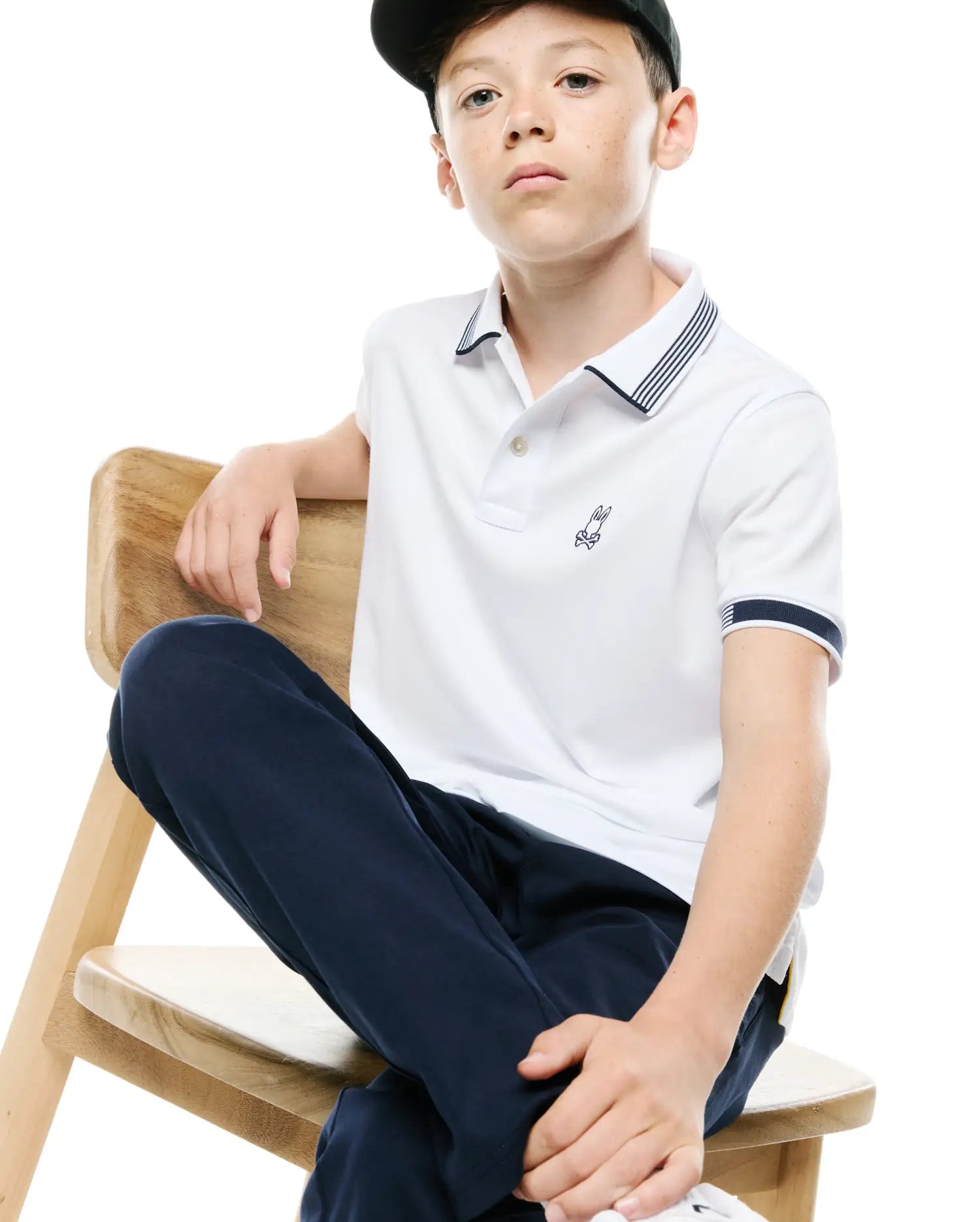 Kids Timmy Pique Polo in white, featuring a classic fit, pique fabric, navy blue striped collar and cuffs, and a small embroidered Psycho Bunny skull logo on the left chest.