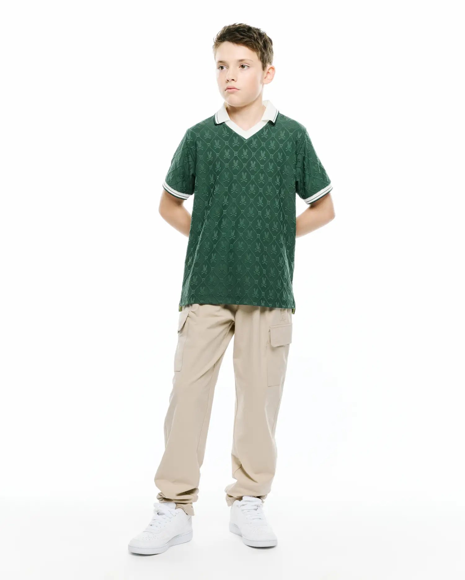 Kids Garry Jacquard Johnny Collar Polo in dark green, featuring an all-over jacquard pattern of small Psycho Bunny skull logos, a white V-neck Johnny collar, and white striped cuffs. Classic fit.