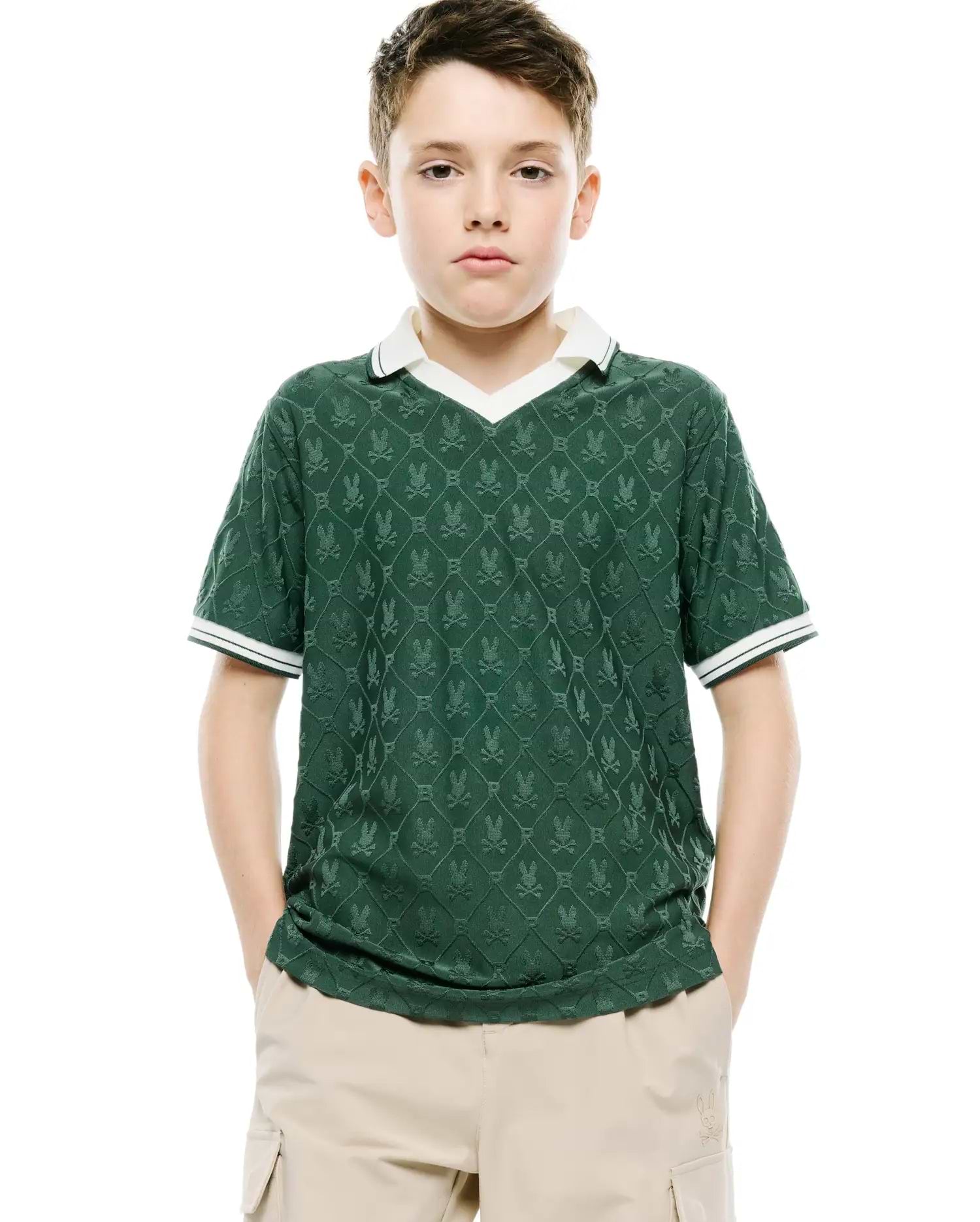Kids Garry Jacquard Johnny Collar Polo, a classic fit dark green jacquard knit polo with an all-over Psycho Bunny skull logo pattern, white V-neck collar, and striped cuffs.