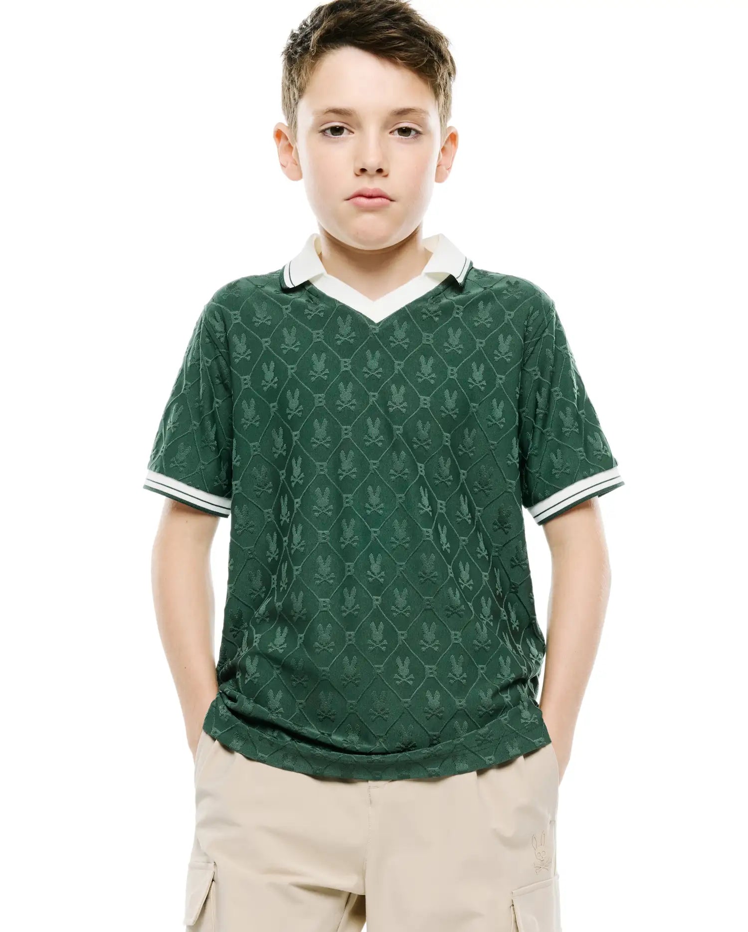 Kids Garry Jacquard Johnny Collar Polo, a classic fit dark green jacquard knit polo with an all-over Psycho Bunny skull logo pattern, white V-neck collar, and striped cuffs.