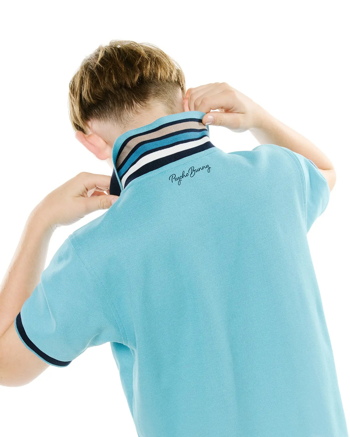 Kids' Klaus Pique Polo in light blue, featuring a classic fit, pique fabric, and a striped collar with navy, white, light blue, and tan accents. Small Psycho Bunny script logo embroidered on the upper back. (3)