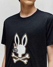 A person wearing the Psycho Bunny KIDS WADE GRAPHIC TEE (KT0200054), a black 100% cotton shirt with a large white bunny head and crossbones graphic and a smaller bunny skull and crossbones on the chest.