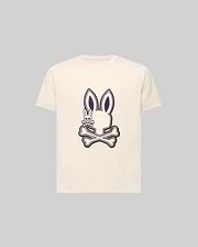 The KIDS WADE GRAPHIC TEE - KT0200054 by Psycho Bunny is a cream-colored 100% cotton tee with a large bunny head and crossbones graphic, plus a small smiling embroidered Bunny on the chest. The background is light gray.