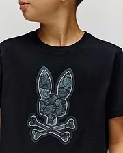 A child in the Psycho Bunny KIDS ROWEN BUNNY GRAPHIC TEE (KT0200058), made in Peru from soft Pima cotton, featuring a large bunny head and crossbones with a textured, floral pattern on the front, looks to the side. (2)
