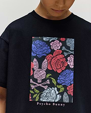 A child wears the Psycho Bunny KIDS ROWEN OVERSIZED TEE—an oversized, relaxed fit tee with a bold floral graphic in red, blue, and purple flowers, green leaves, and the Psycho Bunny logo. "Psycho Bunny" appears below the vibrant design. (2)