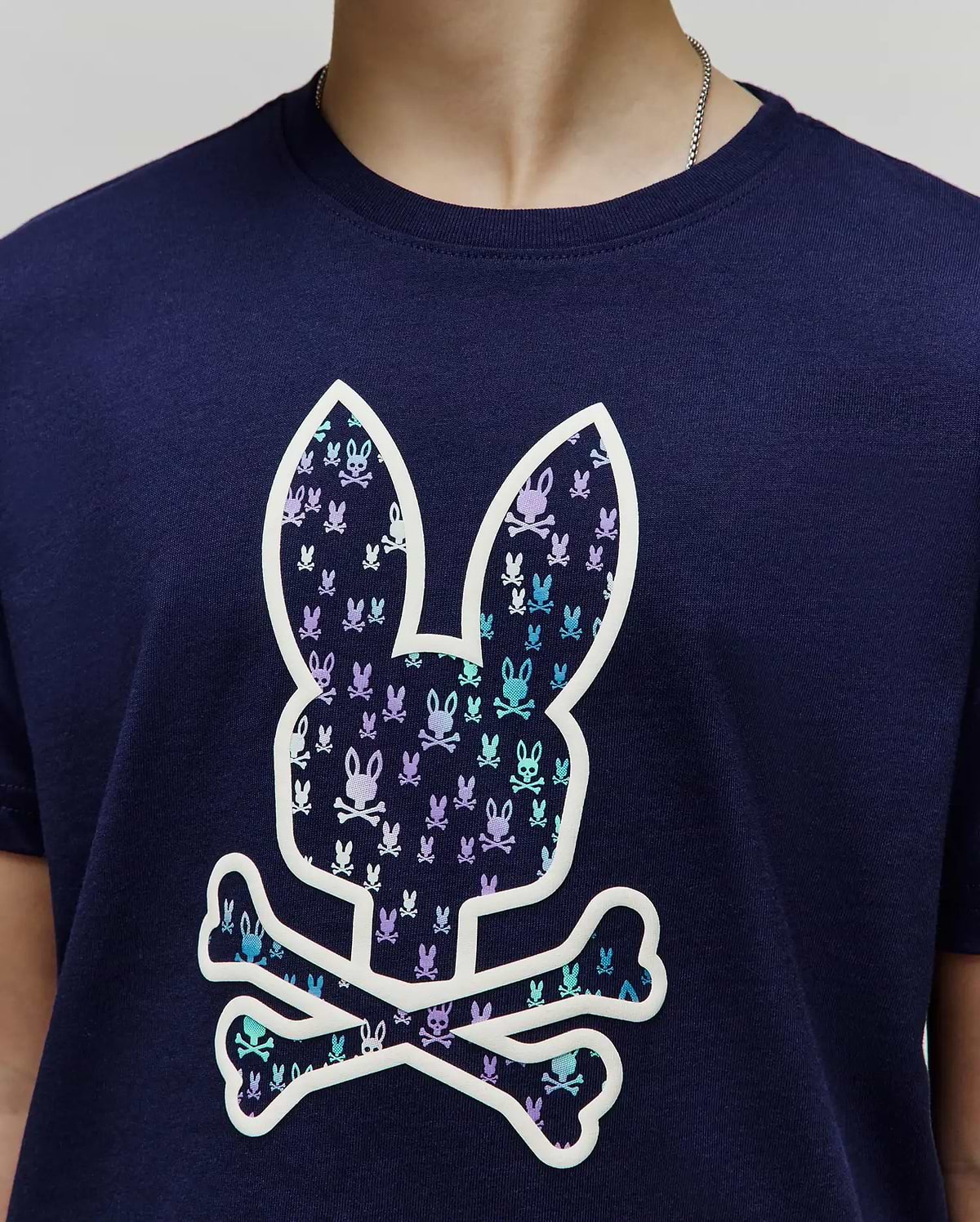 Kids Nev Bunny Graphic Tee. Navy jersey knit, classic fit. Features a large central white-outlined Psycho Bunny skull logo filled with small repeating light blue and purple bunny skulls. (3)