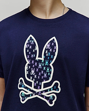 Kids Nev Bunny Graphic Tee. Navy jersey knit, classic fit. Features a large central white-outlined Psycho Bunny skull logo filled with small repeating light blue and purple bunny skulls. (3)