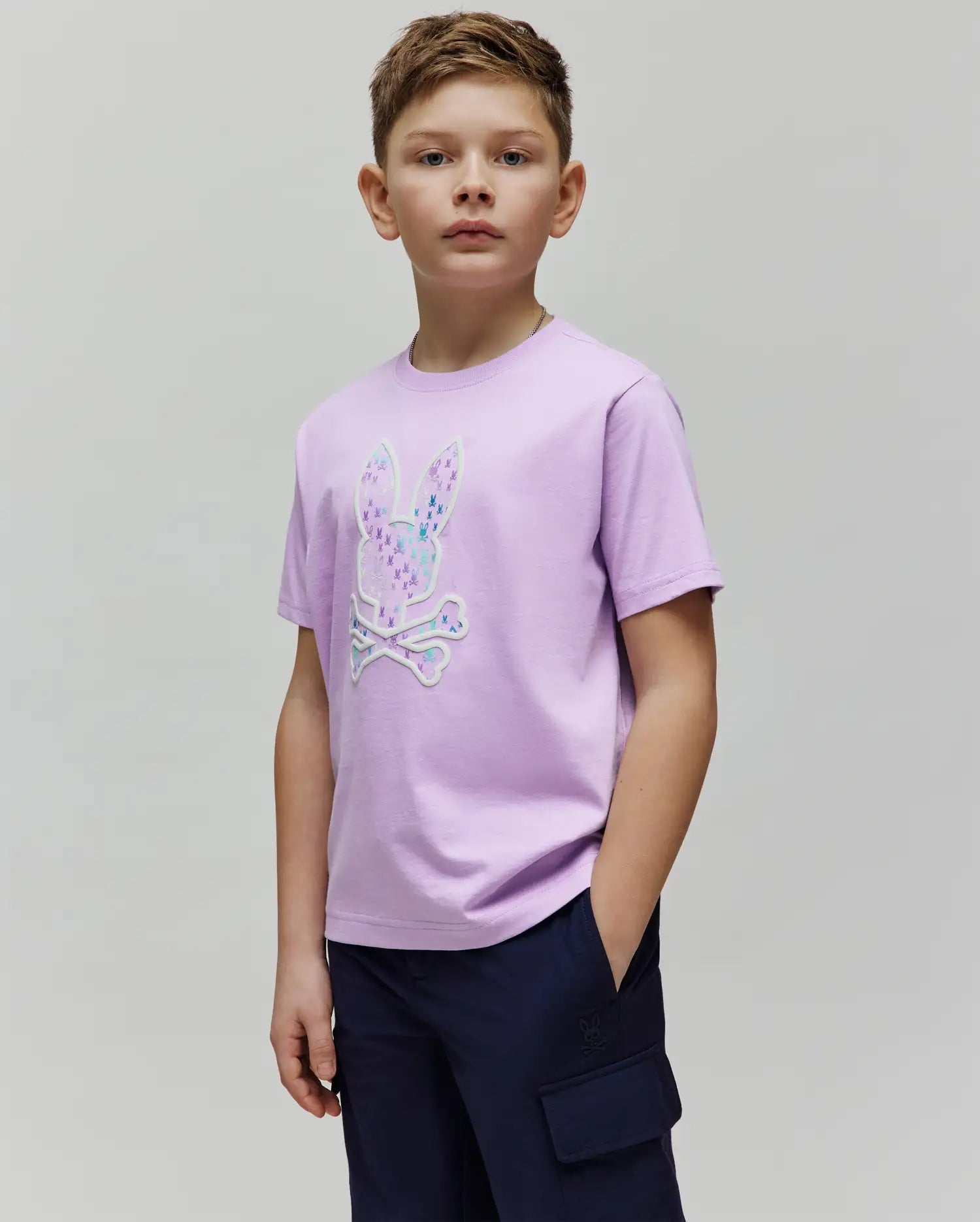 Kids Nev Bunny Graphic Tee, a classic fit lavender jersey t-shirt featuring a large central Psycho Bunny skull logo graphic filled with vibrant multi-color mini bunny patterns and a white outline. (2)
