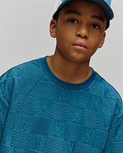 Kids Dustin Oversized Tee in teal, featuring an all-over embossed checkerboard pattern with alternating Psycho Bunny skull logos and textured squares, crafted from a soft, oversized knit fabric.