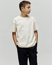 Cream Kids Dustin Oversized Tee with an all-over embossed checkerboard pattern of small Psycho Bunny skull logos and textured squares.