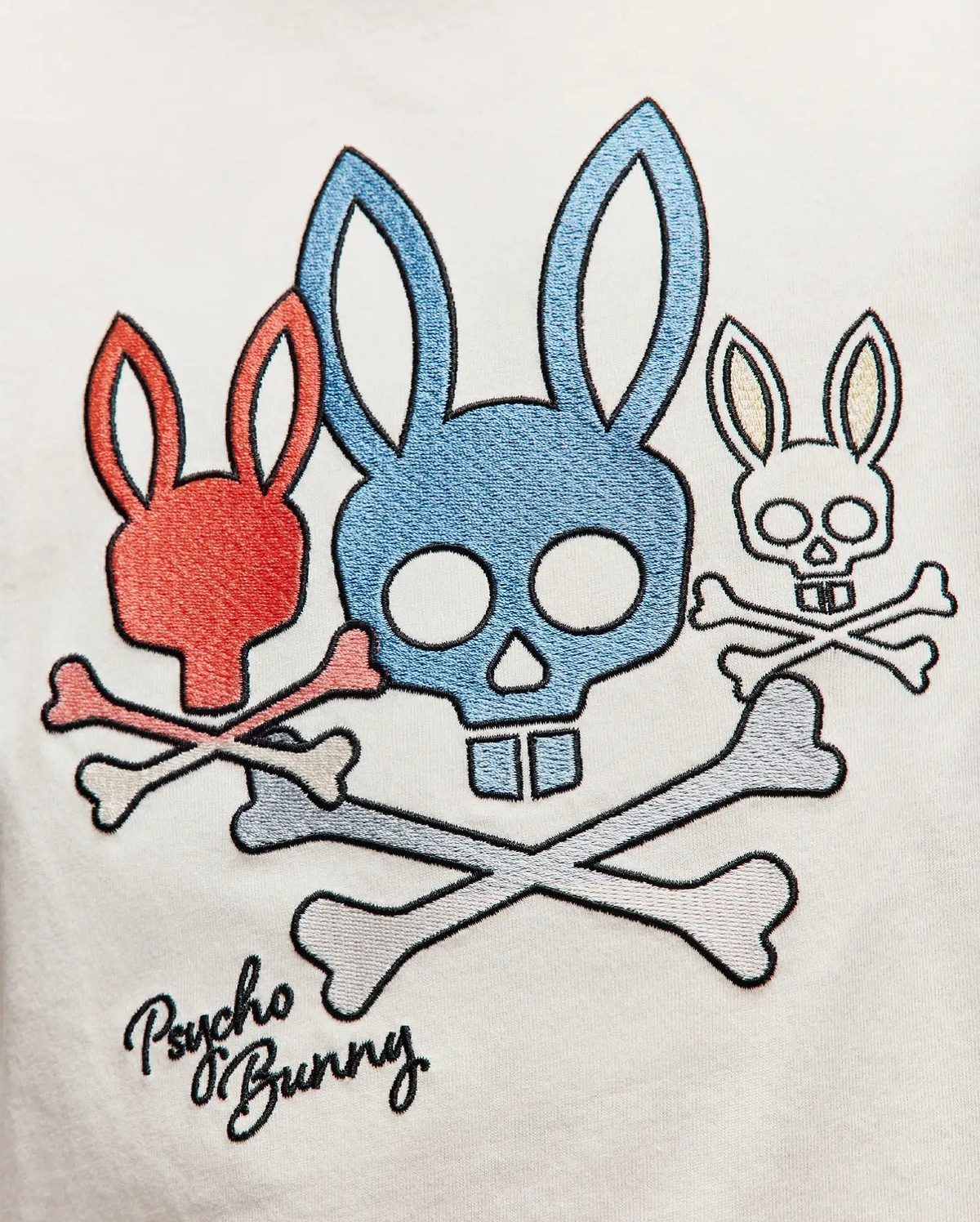 Kids Oscar Graphic Tee in white jersey, featuring a central embroidered graphic of three bunny skulls: large blue, smaller red, and small white, all with crossed bones, and black Psycho Bunny script below. (3)