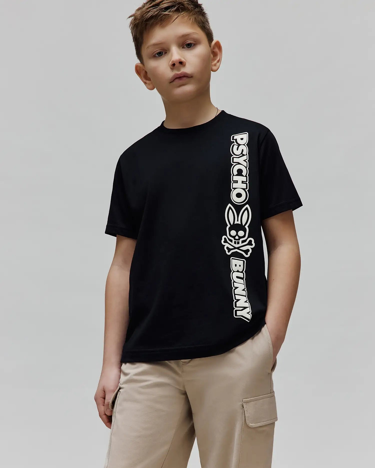 Kids Toby Wordmark Tee, a black classic fit jersey knit t-shirt featuring a large vertical white Psycho Bunny wordmark and iconic bunny skull logo graphic on the left side.