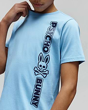 Light blue Kids Toby Wordmark Tee, a classic fit jersey t-shirt featuring a prominent vertical dark blue Psycho Bunny wordmark and iconic bunny skull logo graphic on the front.