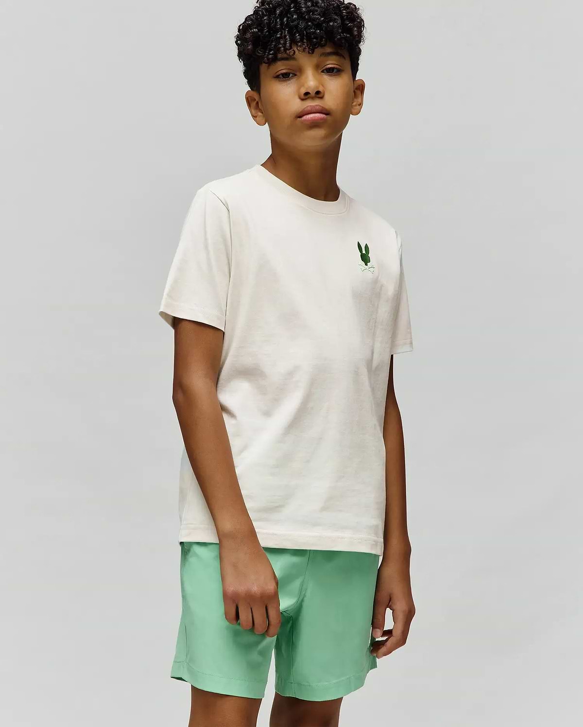 Kids Aiden Back Graphic Tee, classic fit cream jersey t-shirt with a small embroidered green Psycho Bunny skull logo on the left chest, paired with mint green shorts.