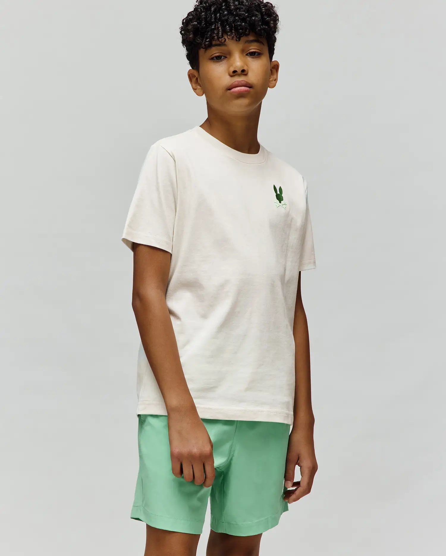 Kids Aiden Back Graphic Tee, classic fit cream jersey t-shirt with a small embroidered green Psycho Bunny skull logo on the left chest, paired with mint green shorts.