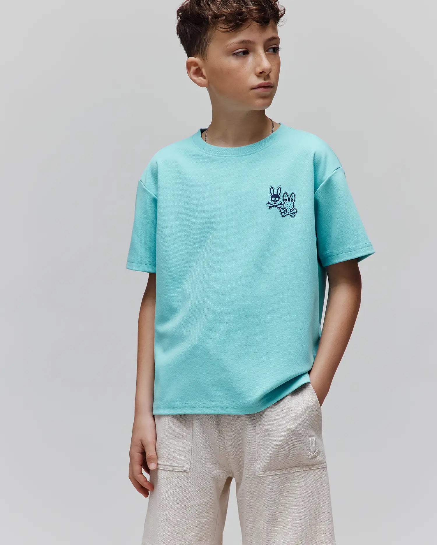 Kids Luke Back Graphic Tee in aqua pique knit, featuring a relaxed fit and two small, embroidered dark blue Psycho Bunny skull and crossbones logos on the left chest.