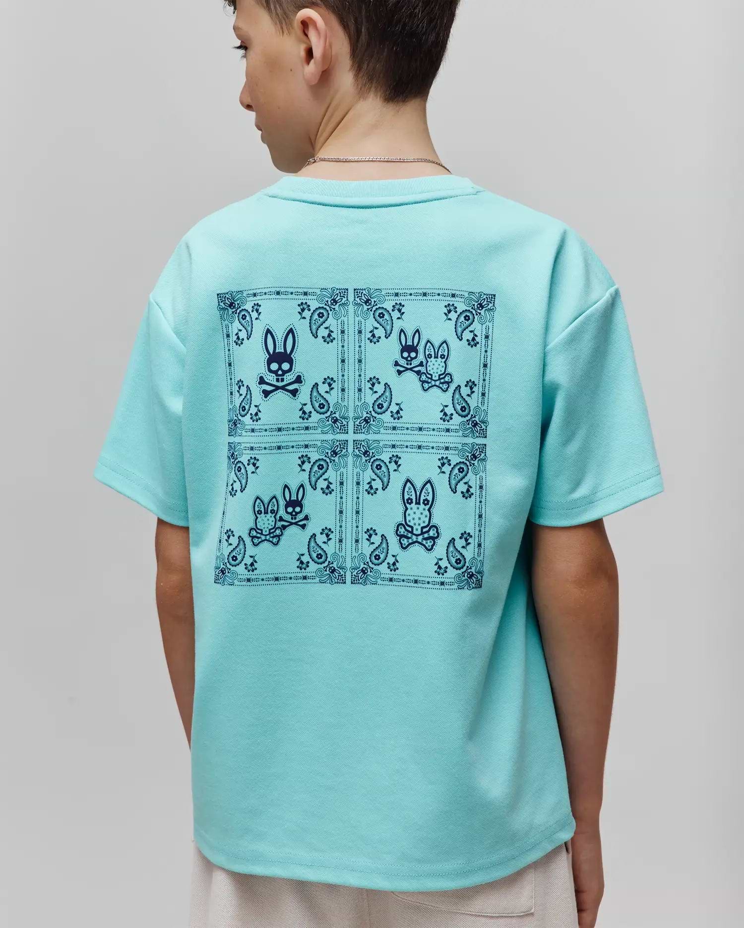 Kids Luke Back Graphic Tee in aqua, featuring a relaxed fit and smooth jersey knit. A large dark blue back graphic displays four squares with bandana borders, paisley patterns, and the iconic Psycho Bunny skull logo.