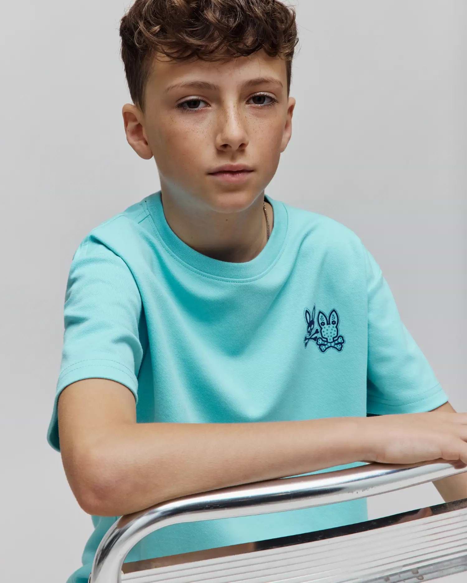 Kids Luke Back Graphic Tee in aqua smooth jersey, featuring a classic fit and a small, dark blue embroidered Psycho Bunny skull logo on the left chest.