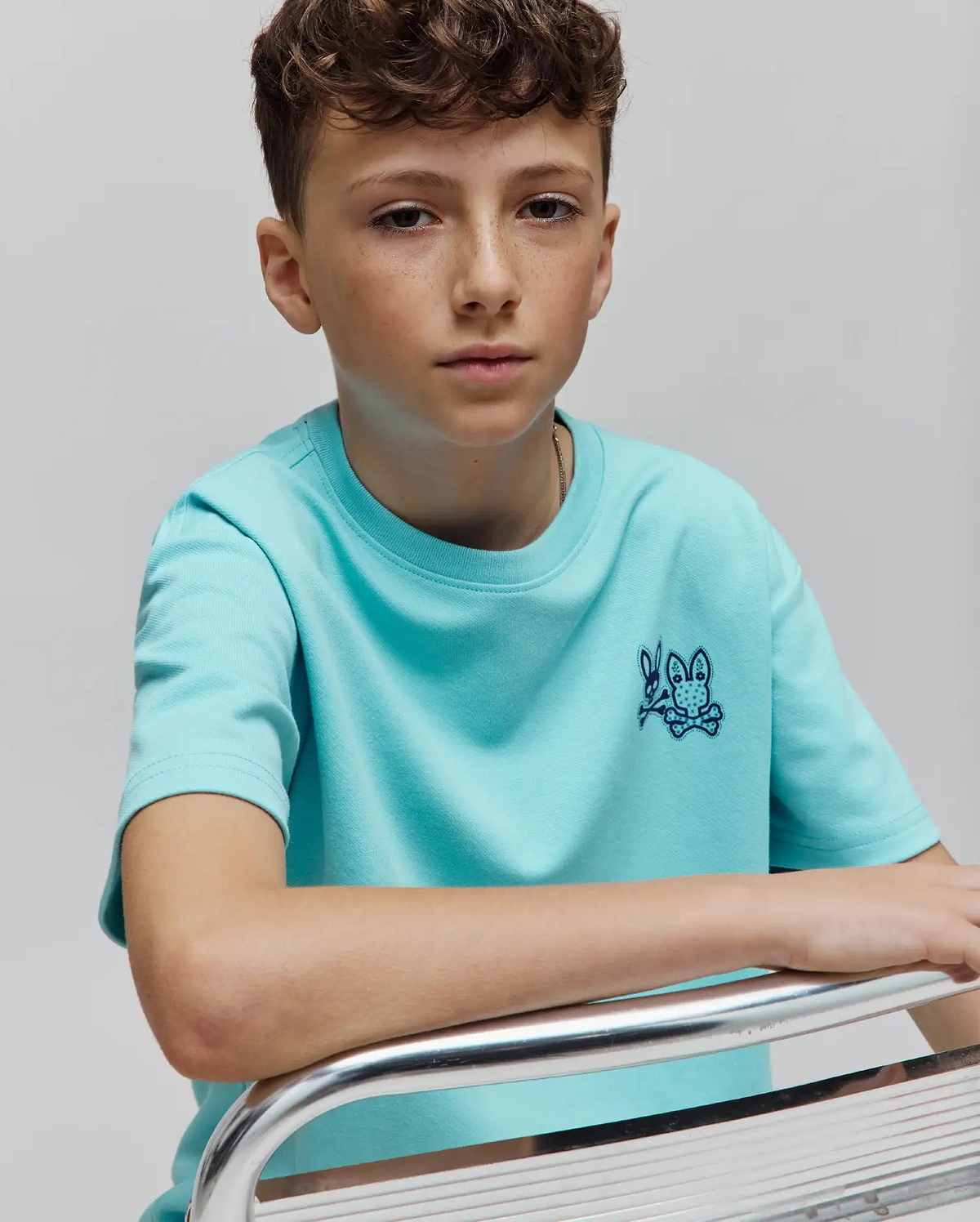 Kids Luke Back Graphic Tee in aqua smooth jersey, featuring a classic fit and a small, dark blue embroidered Psycho Bunny skull logo on the left chest.