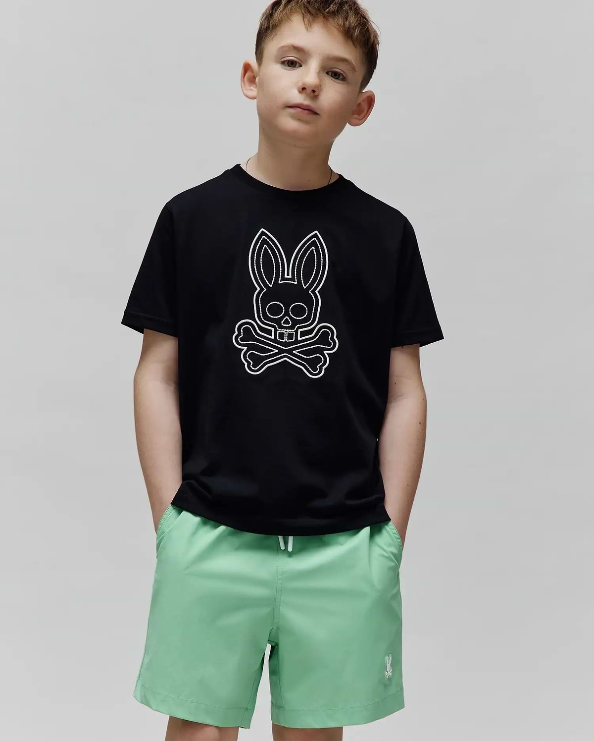 Black jersey Kids Marcel Graphic Tee with a classic fit, featuring a large white outline Psycho Bunny skull and crossbones graphic centered on the chest, paired with mint green shorts.