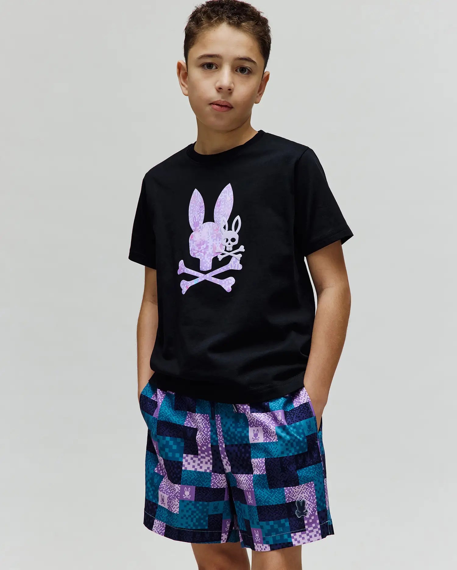 Black Kids Van Graphic Tee, classic fit jersey, with a large pixelated purple and white Psycho Bunny skull chest graphic. Paired with multi-color checkered woven shorts featuring integrated bunny logos. (2)