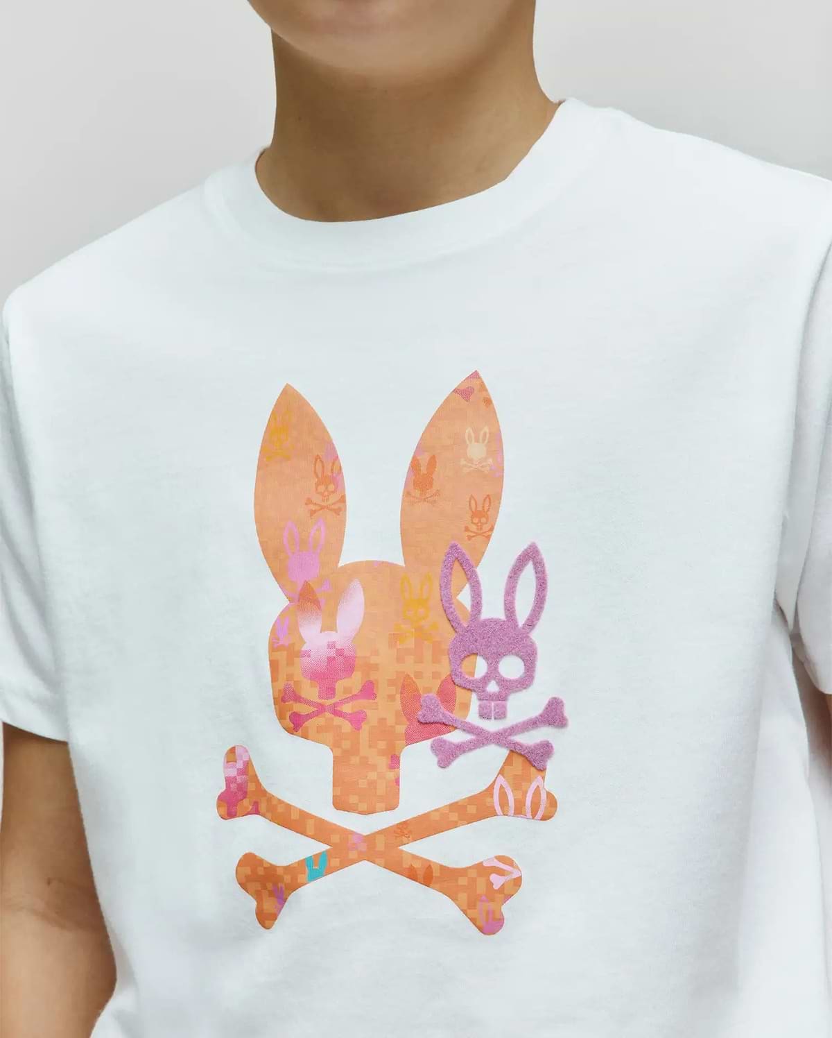 Kids Van Graphic Tee, a white classic fit jersey t-shirt featuring a large chest graphic of an orange pixelated bunny skull with ears and crossbones, subtly patterned with mini bunny skulls, overlaid by a smaller purple felt bunny skull. (3)