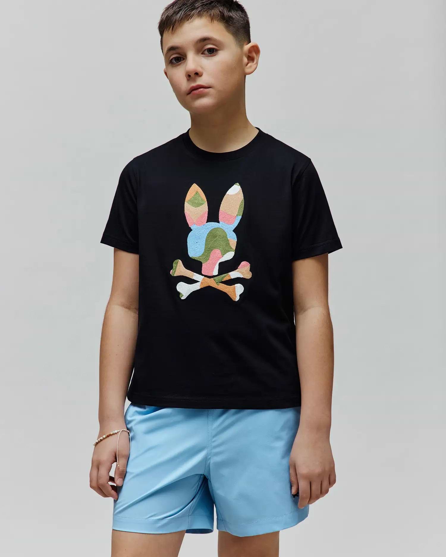 Kids Ara Graphic Tee, a black classic fit jersey t-shirt with a large central graphic of the iconic Psycho Bunny skull and crossbones logo in a vibrant multi-color camouflage pattern.