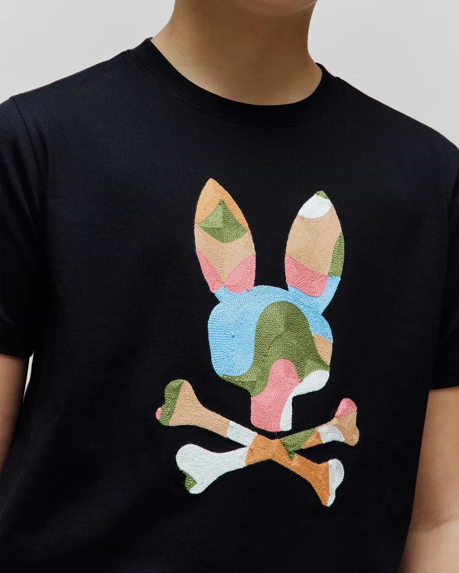 Kids Ara Graphic Tee: Black jersey t-shirt with a large, central embroidered Psycho Bunny skull logo featuring a vibrant, multi-colored abstract pattern in pink, blue, green, orange, and white.