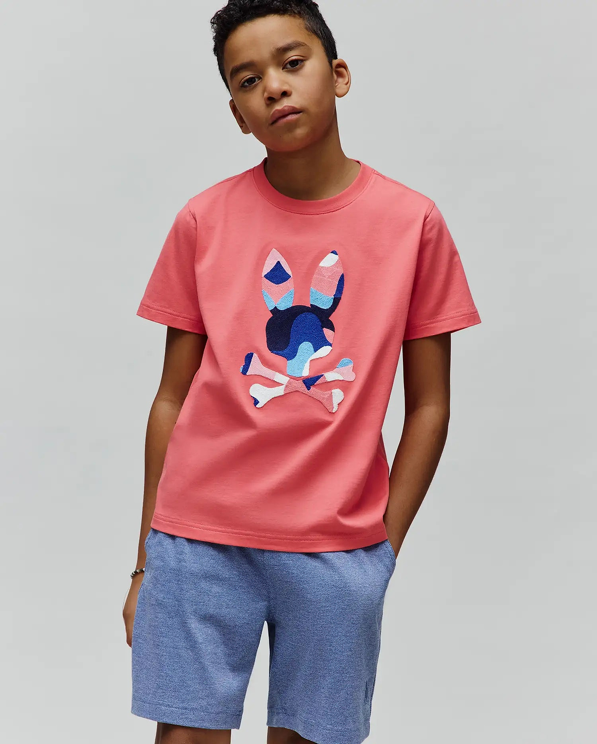 Coral Pink Kids Ara Graphic Tee in classic fit jersey, featuring a large, vibrant blue and white patterned Psycho Bunny skull logo on the center chest.