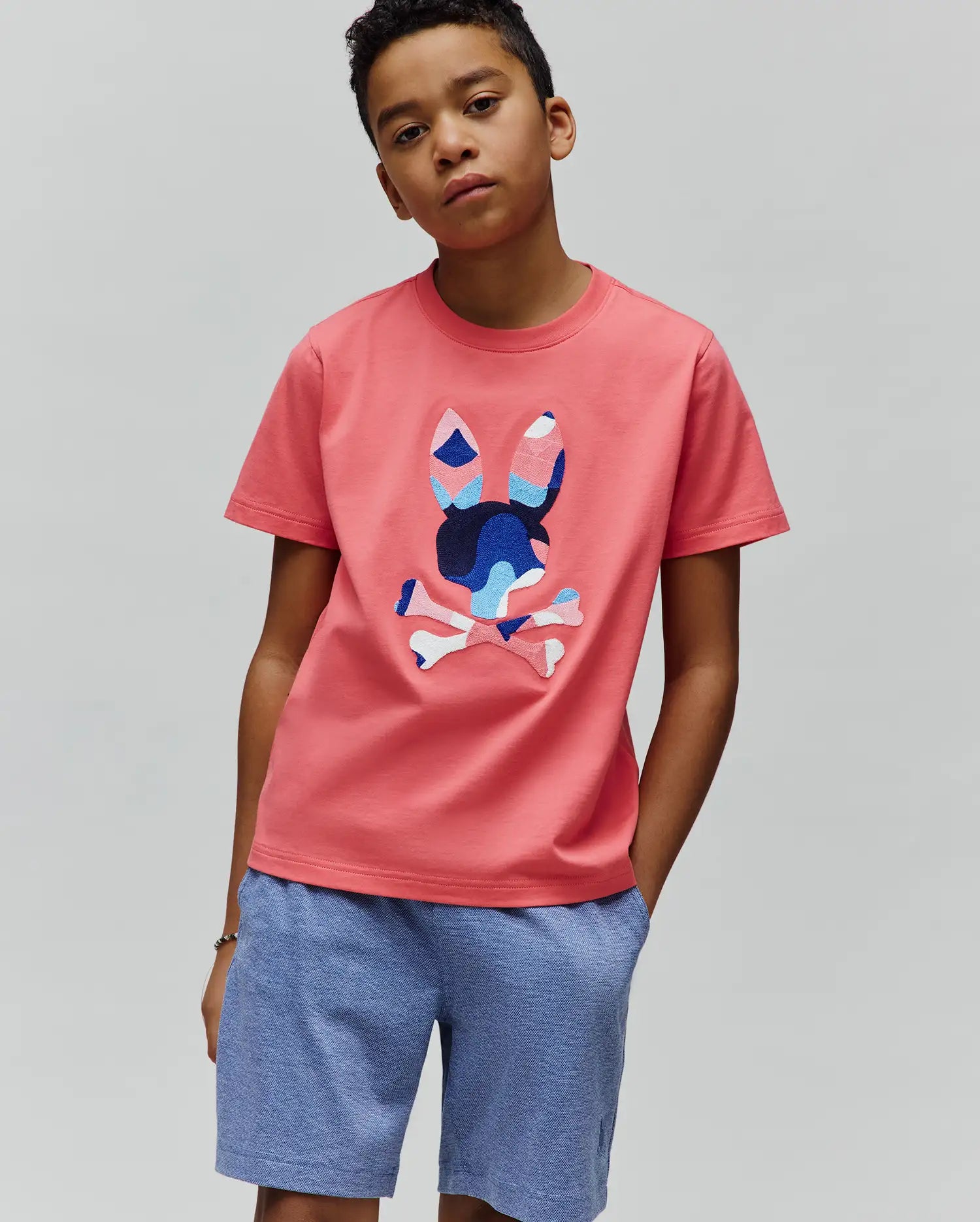 Coral Pink Kids Ara Graphic Tee in classic fit jersey, featuring a large, vibrant blue and white patterned Psycho Bunny skull logo on the center chest.