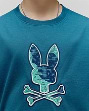 Kids Olivier Graphic Tee, a classic fit teal jersey knit t-shirt with a large central chest embroidered Psycho Bunny skull logo featuring a cross-stitch pattern in dark blue and light green, outlined in white. (3)