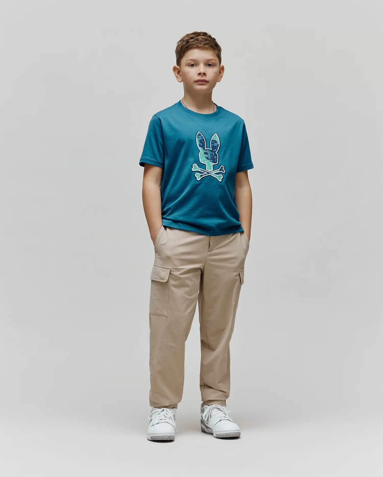 Kids Olivier Graphic Tee in teal jersey, featuring a large, textured blue and green Psycho Bunny skull and crossbones graphic on the chest, paired with relaxed fit khaki cargo pants. (4)