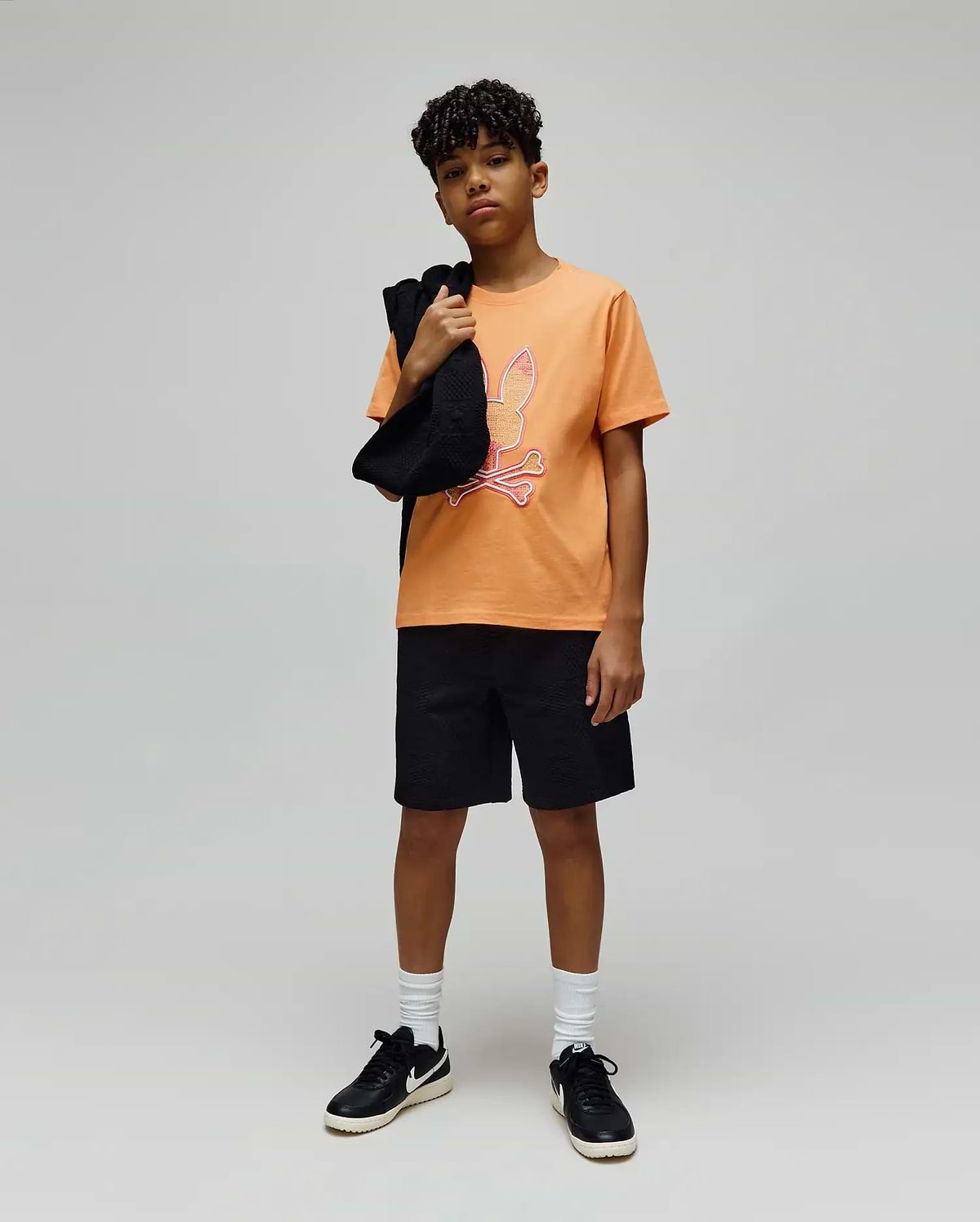Kids Olivier Graphic Tee in vibrant orange jersey, featuring a large pink and white Psycho Bunny skull logo graphic on the chest, paired with black textured shorts for a relaxed fit. (4)