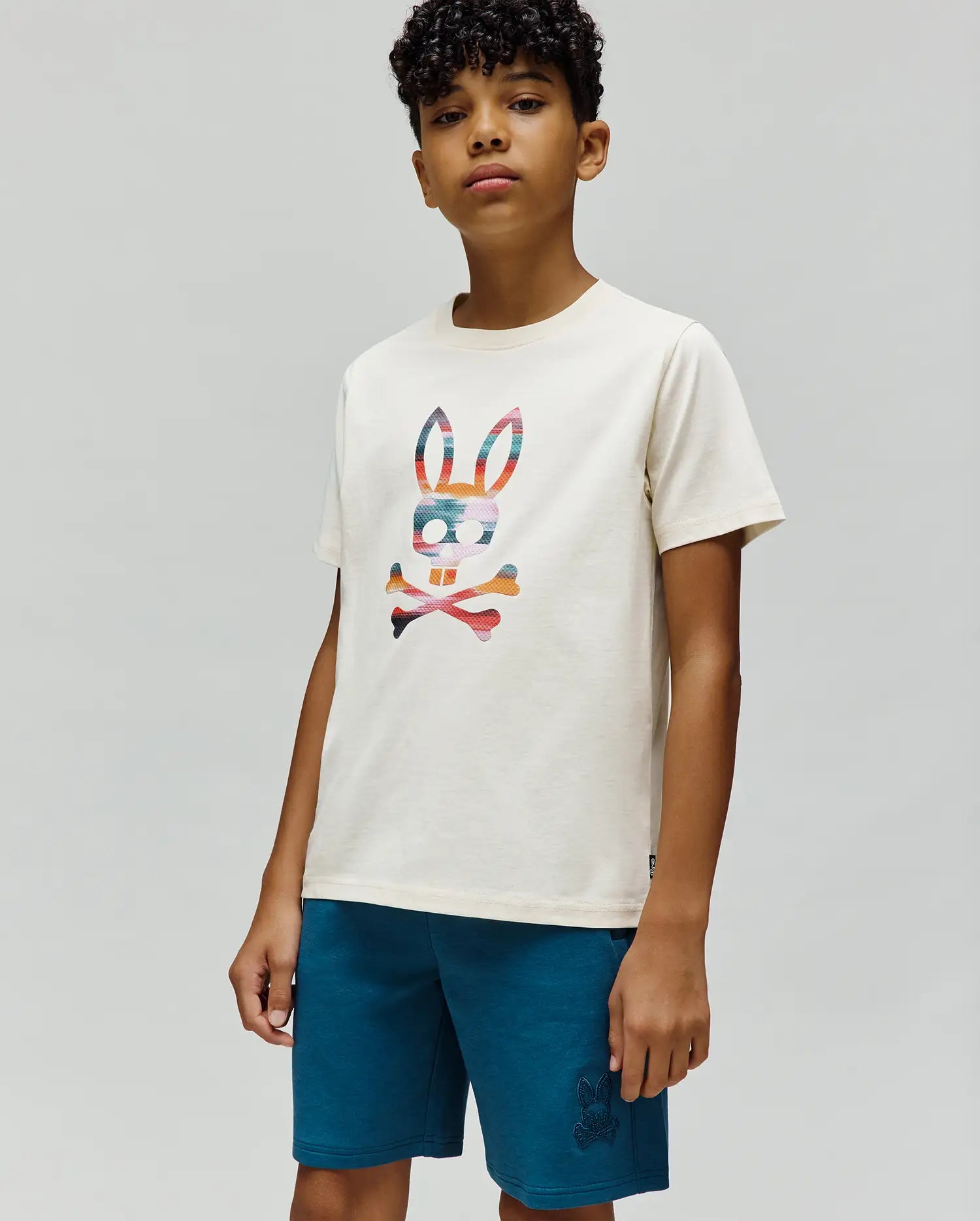 Kids Raphael Graphic Tee, an ecru jersey knit with a classic fit, showcasing a large, vibrant multi-color striped Psycho Bunny skull graphic on the chest.