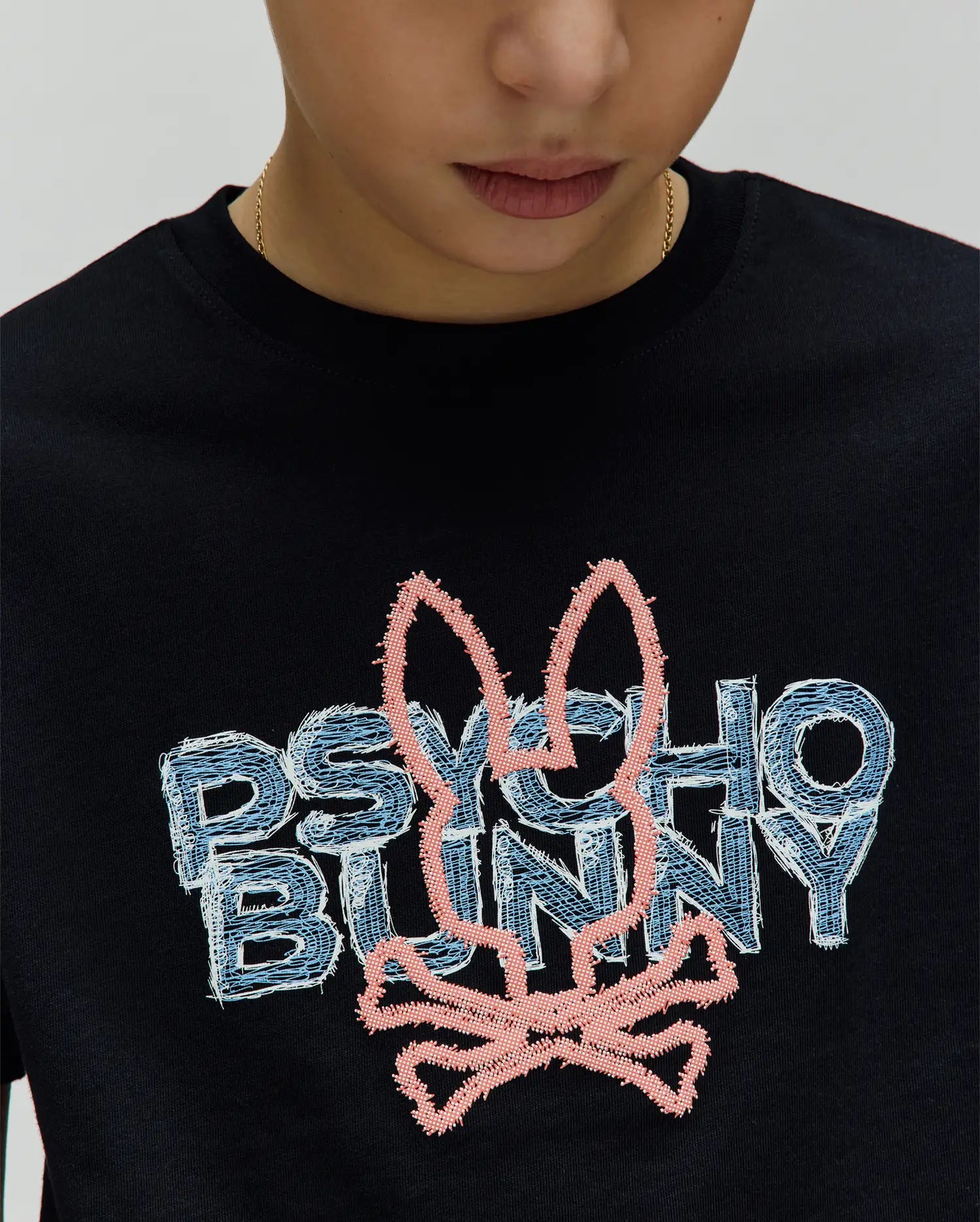 Kids Herman Graphic Tee. Black classic fit jersey t-shirt with a large central embroidered Psycho Bunny logo featuring light blue/white distressed text and a pink textured bunny skull.