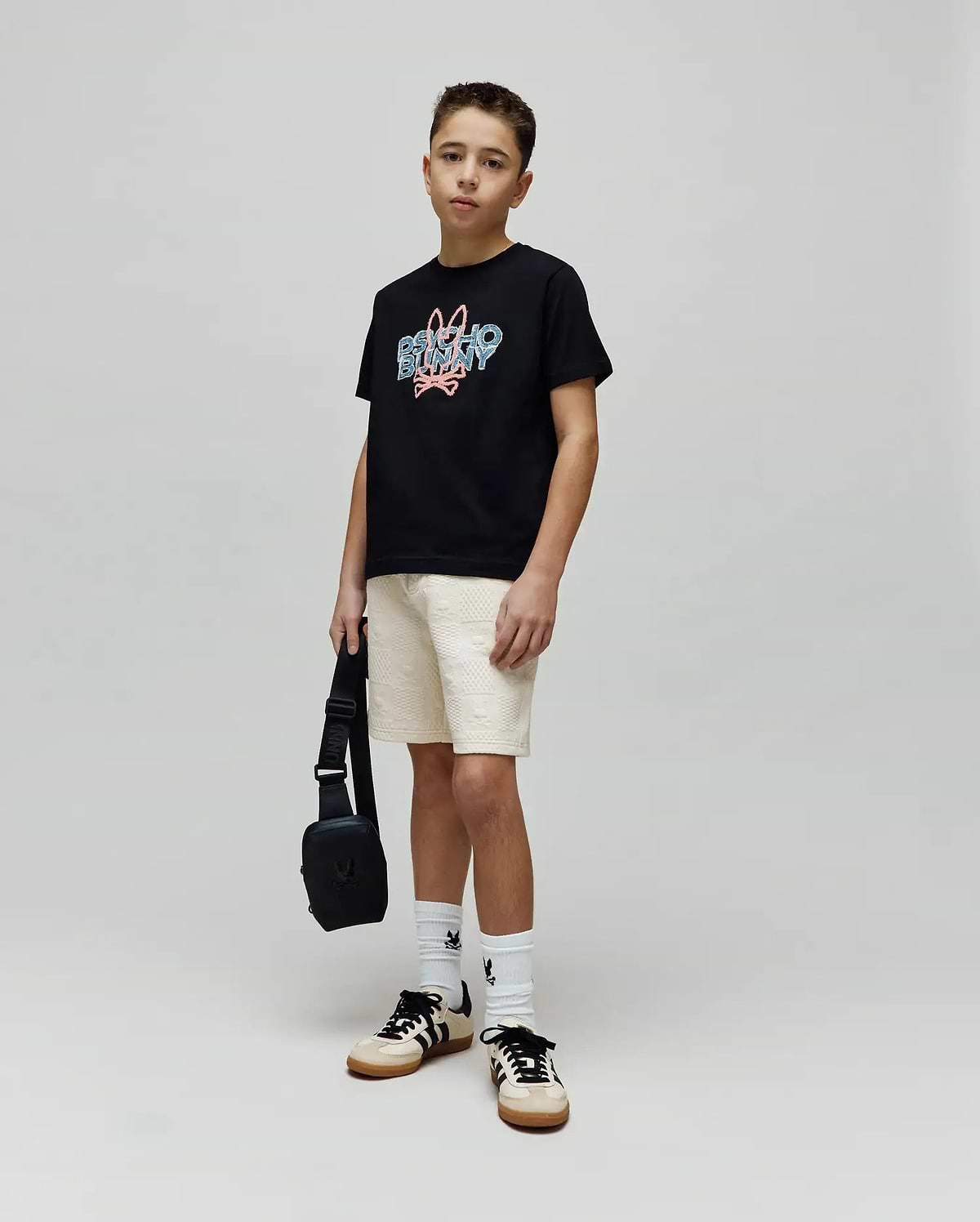 Kids Herman Graphic Tee, a black classic fit cotton jersey t-shirt featuring a large central chest graphic of the Psycho Bunny logo and text in blue and pink distressed print.
