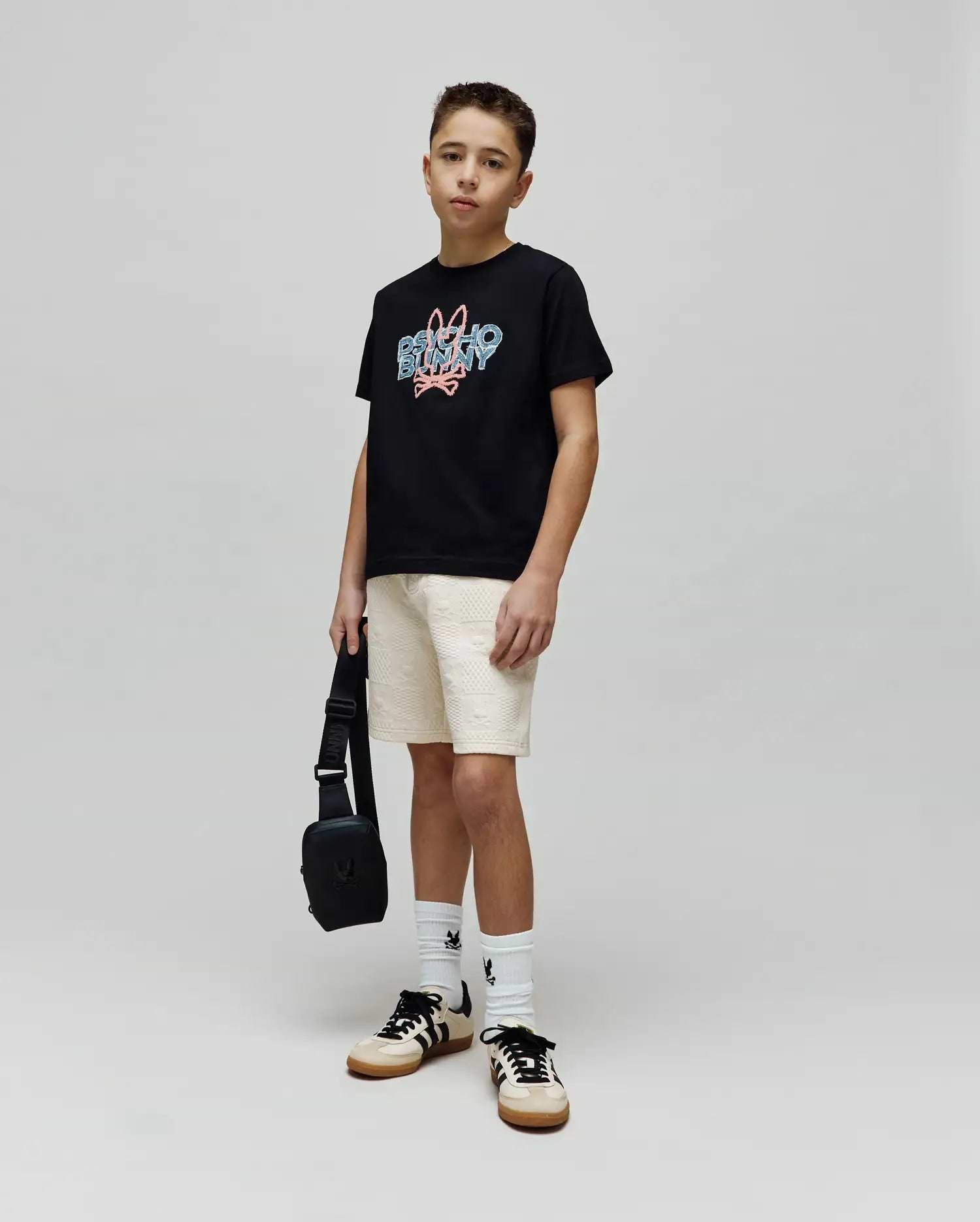 Kids Herman Graphic Tee, a black classic fit cotton jersey t-shirt featuring a large central chest graphic of the Psycho Bunny logo and text in blue and pink distressed print.