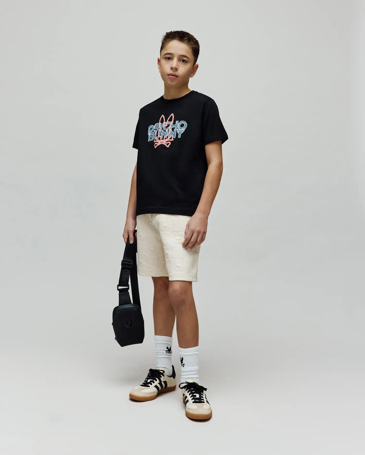 Kids Herman Graphic Tee, a black classic fit cotton jersey t-shirt featuring a large central chest graphic of the Psycho Bunny logo and text in blue and pink distressed print.