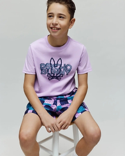 Kids Herman Graphic Tee, a classic fit lilac jersey t-shirt featuring a large central textured Psycho Bunny skull logo and text graphic, paired with relaxed geometric patchwork shorts in purple, teal, and blue. (4)
