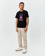 Kids Adler Graphic Tee, a black cotton jersey t-shirt with a large pink Psycho Bunny skull and crossbones logo and text on the chest, styled with beige cargo pants.