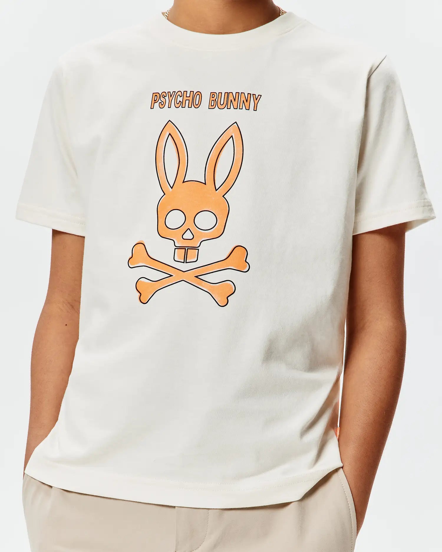 Kids Adler Graphic Tee, a cream classic fit jersey t-shirt with a large central orange and black Psycho Bunny skull and crossbones graphic and PSYCHO BUNNY text.