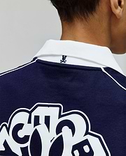 Kids Toby Jersey navy blue jersey polo, with a white ribbed collar, white shoulder piping, small embroidered Psycho Bunny skull logo on the back collar, and large white graphic print on the back.