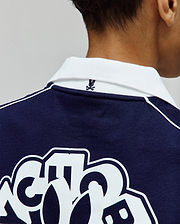 Kids Toby Jersey navy blue jersey polo, with a white ribbed collar, white shoulder piping, small embroidered Psycho Bunny skull logo on the back collar, and large white graphic print on the back.
