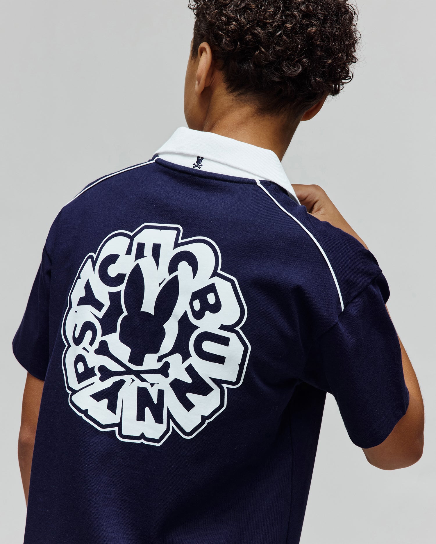 Kids Toby Jersey navy blue classic fit polo shirt with white collar, white shoulder piping, small embroidered bunny skull on collar, and large white Psycho Bunny text and skull graphic on back.