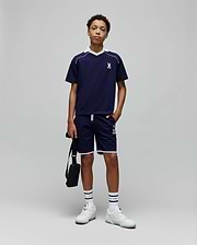 Navy blue Kids Toby Jersey t-shirt with white V-neck collar, shoulder stripe, and small embroidered Psycho Bunny skull logo on the left chest, paired with matching shorts featuring white piping and a large logo print.