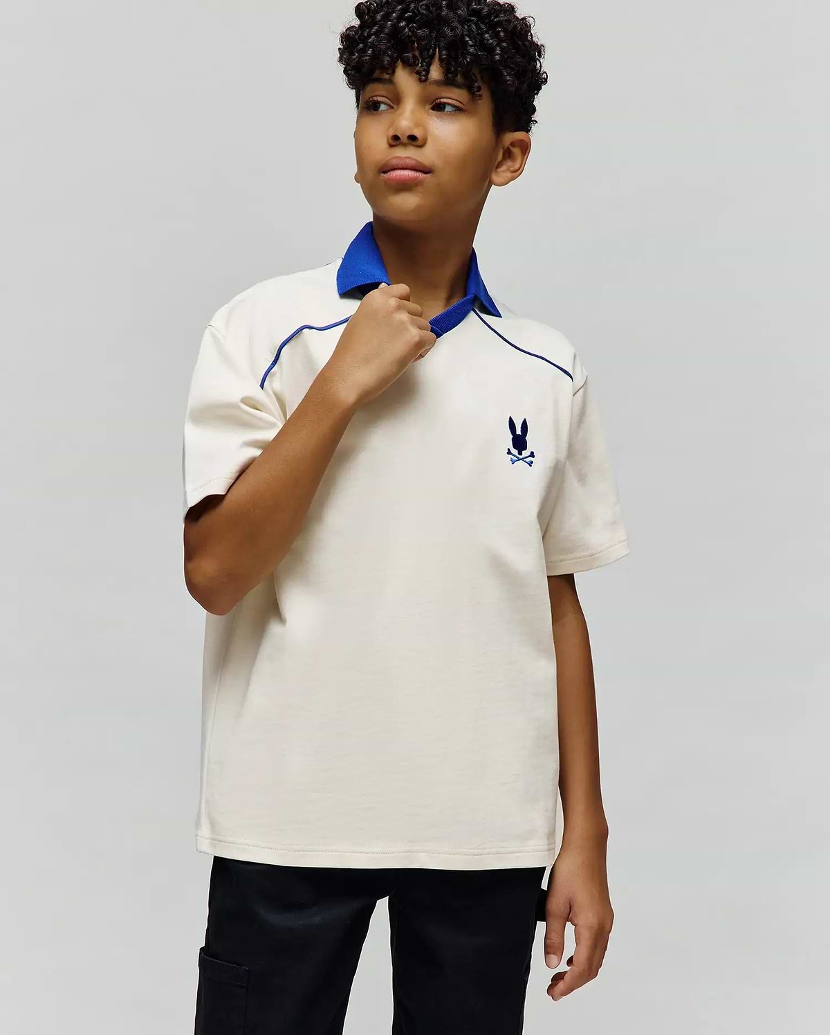 Kids Toby Jersey, a classic fit cream jersey polo with a royal blue collar and V-neck, featuring blue piping details and a small embroidered Psycho Bunny skull logo on the left chest.