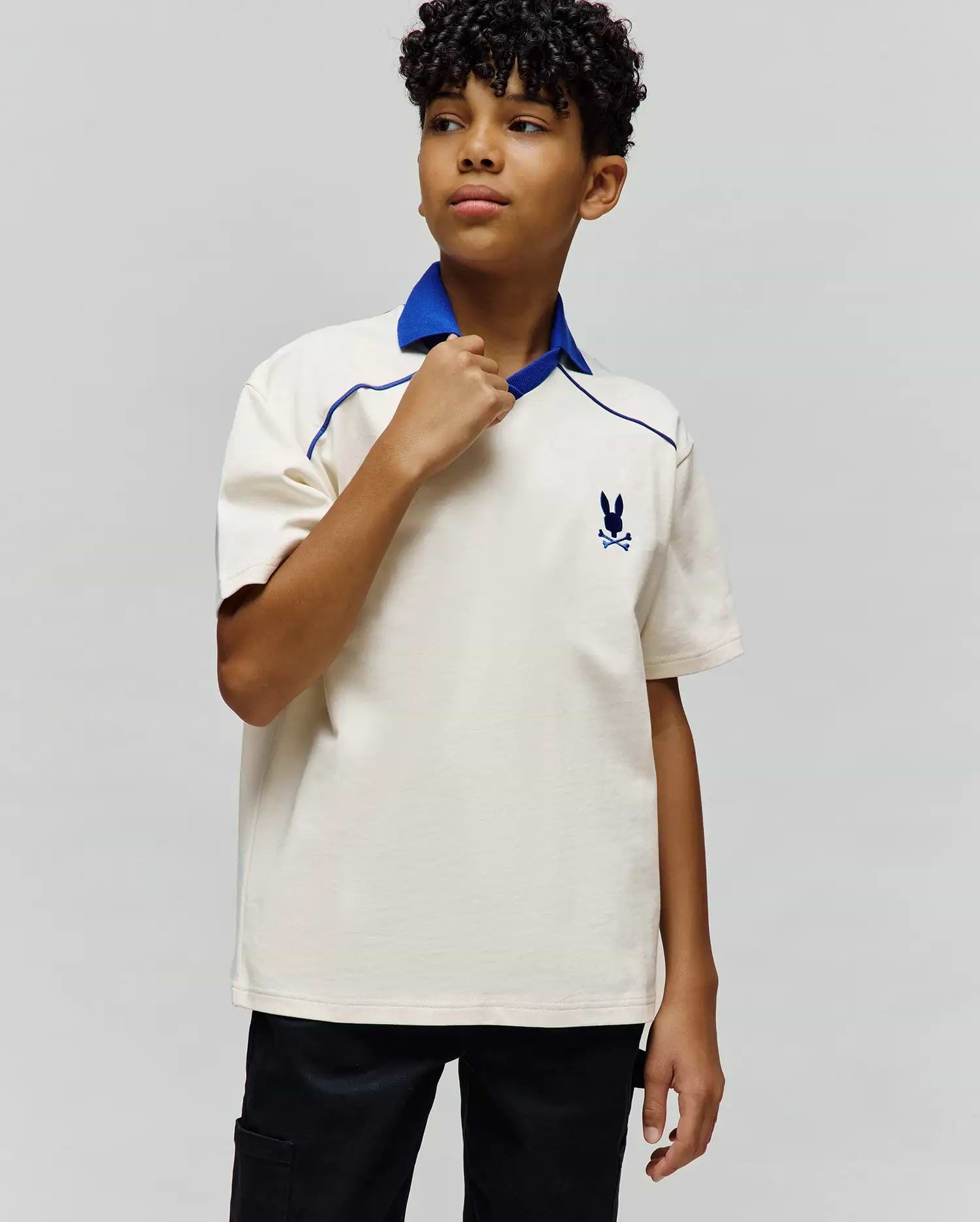 Kids Toby Jersey, a classic fit cream jersey polo with a royal blue collar and V-neck, featuring blue piping details and a small embroidered Psycho Bunny skull logo on the left chest.