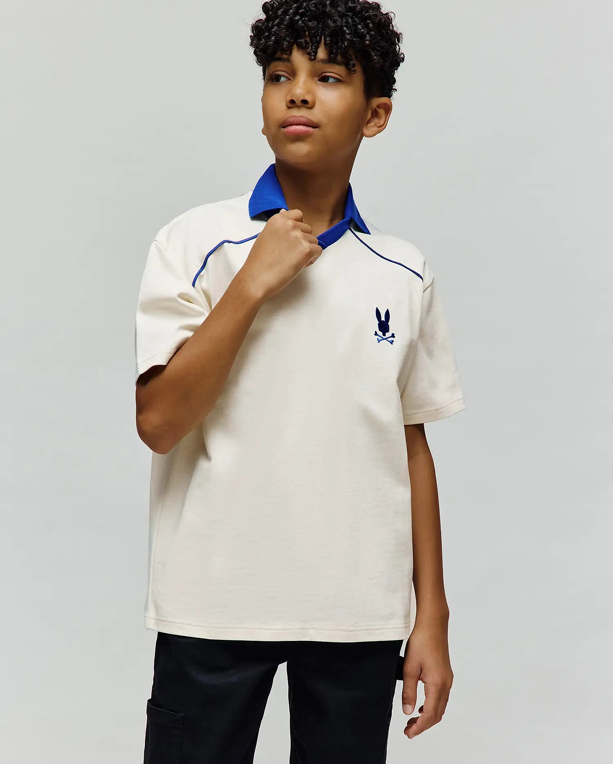 Kids Toby Jersey, a classic fit cream jersey polo with a royal blue collar and V-neck, featuring blue piping details and a small embroidered Psycho Bunny skull logo on the left chest.