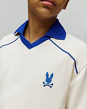 Kids Toby Jersey, cream jersey knit polo with royal blue ribbed collar, V-neck trim, raglan piping, and small embroidered royal blue Psycho Bunny skull logo on left chest.